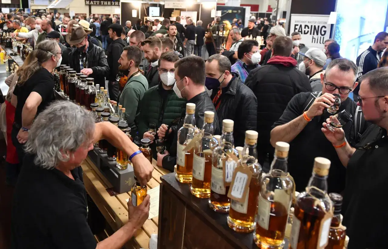 Besucher probieren bei einer Whisky Messe verschiedene Sorten. Viele Flaschen stehen bereit.