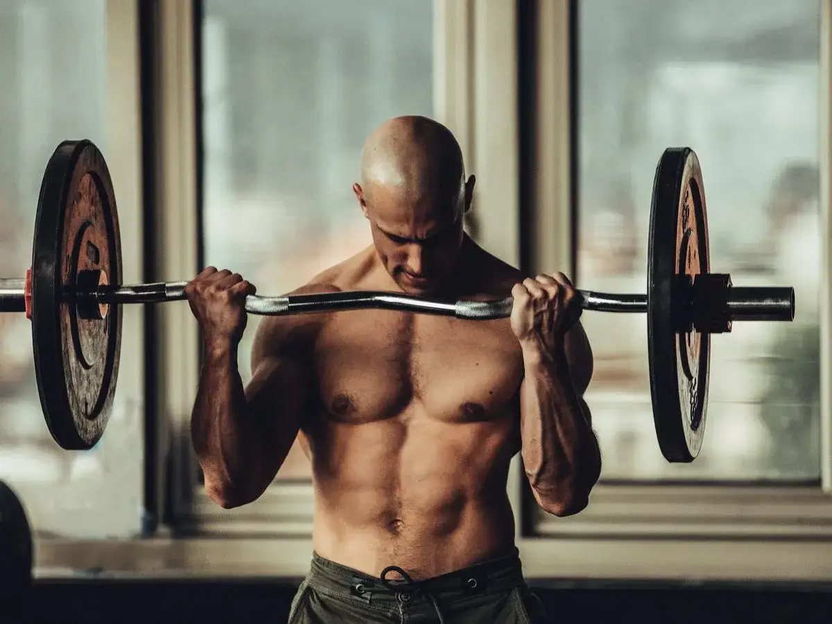 Mężczyzna wykonuje ćwiczenie na biceps z użyciem sztangi. To kluczowy element każdego planu treningowego na biceps.