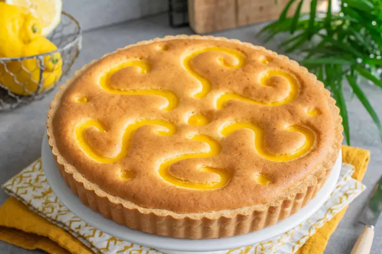 Torta con decorazioni a spirale di crema al limone, su un piatto bianco, con limoni freschi sullo sfondo.