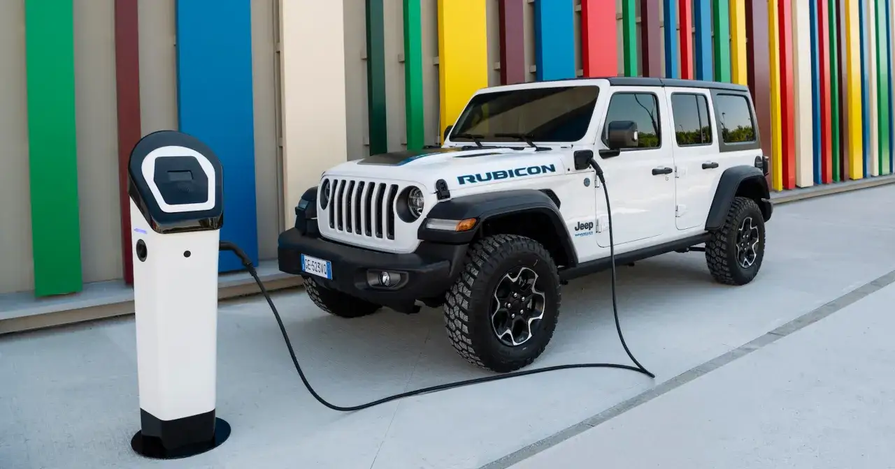 Biały Jeep Wrangler 4xe Rubicon podłączony do ładowarki na tle kolorowych pionowych paneli.