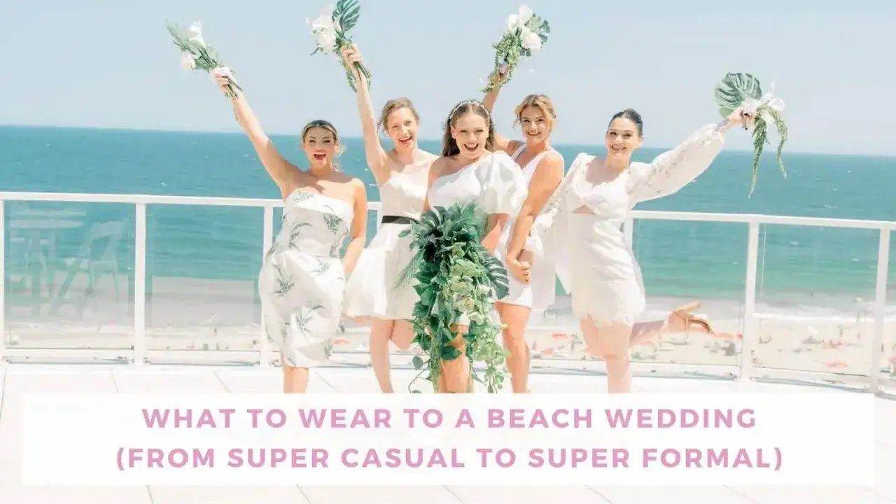Five women in white dresses, holding bouquets, celebrate beach wedding attire with the ocean in the background.