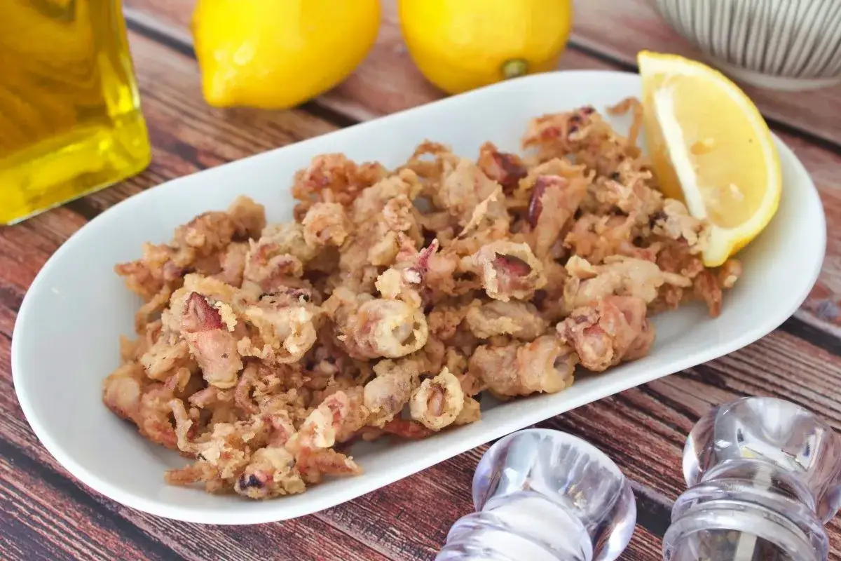 Crujientes puntillas de calamar fritas en un plato blanco, acompa&ntilde;adas de lim&oacute;n y aceite de oliva.