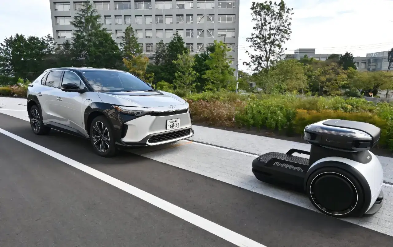 Srebrny, nowoczesny japoński samochód elektryczny obok autonomicznego robota dostawczego.