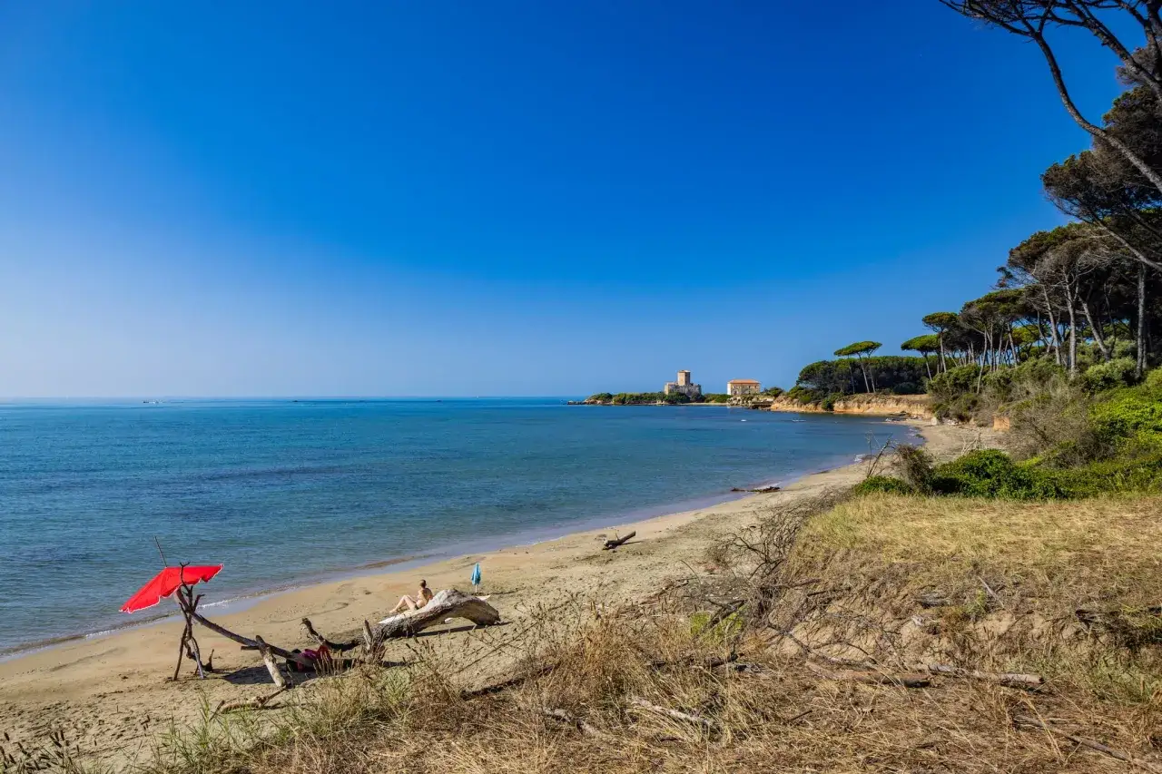 Spiaggia di Torre Astura con un ombrellone rosso, una persona che prende il sole e la torre in lontananza.
