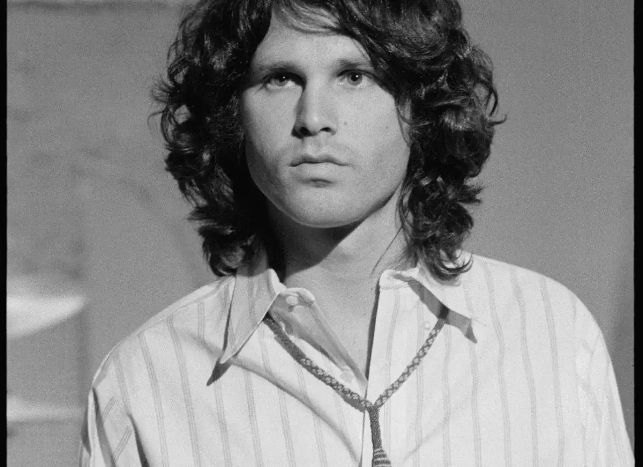 Jim Morrison, wokalista The Doors, w białej koszuli w paski i z naszyjnikiem. Jego spojrzenie jest intensywne, jakby patrzył wprost w **the end the doors**.
