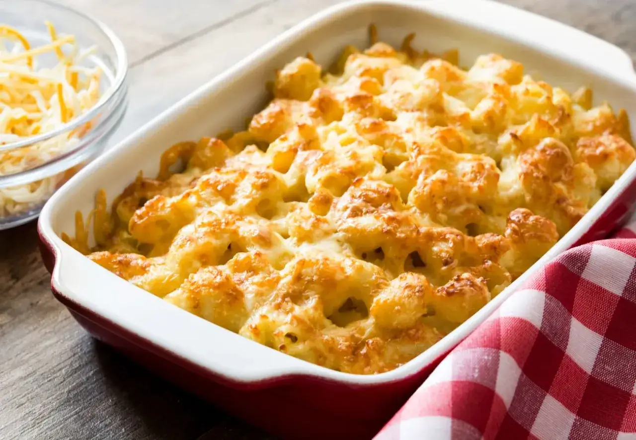 Macarrones con queso recién horneados, dorados y burbujeantes en una fuente roja. Un tazón de queso rallado al lado.