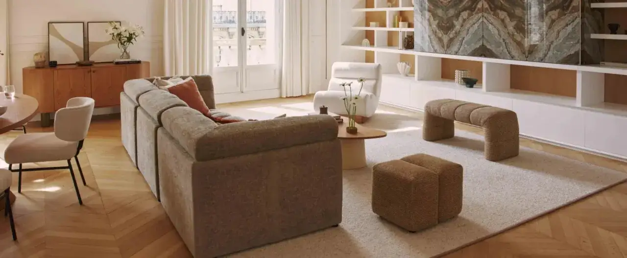 Un soggiorno luminoso con divano modulare, poltrona soffice, tavolino rotondo e pouf coordinati. Un esempio di arredamento contemporaneo chic con toni neutri e texture accoglienti.