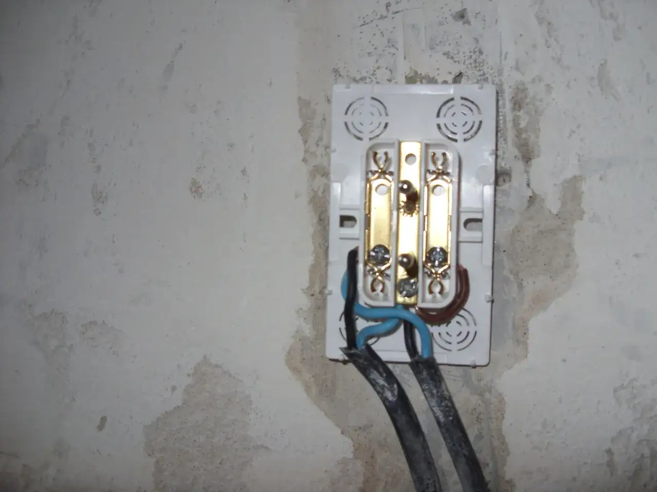 Widoczne przyłącze elektryczne z przewodami. Widać potencjalne małe napięcie na przewodzie neutralnym, co może być niebezpieczne.
