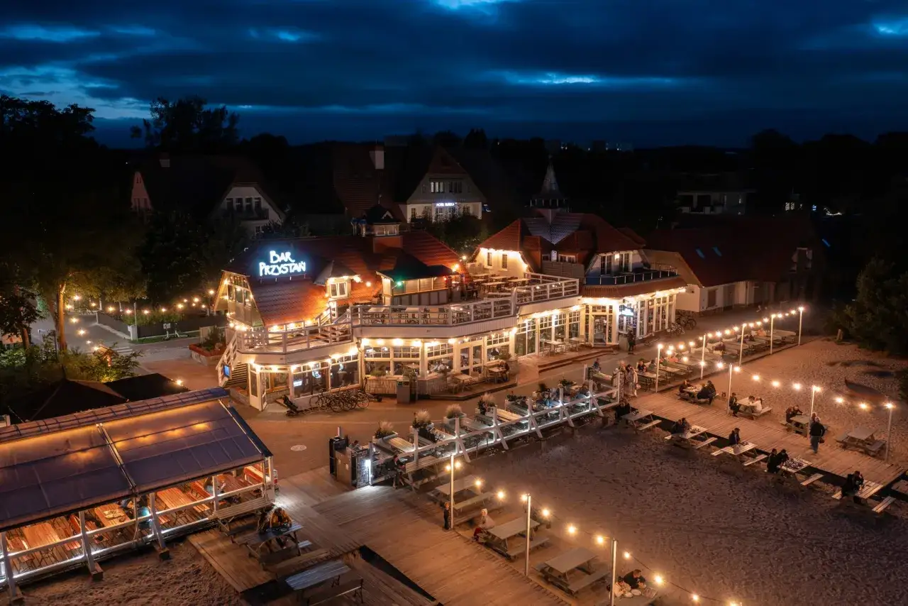 Bar Przystań nocą, gdzie serwują najlepszą rybę w Sopocie. Rozświetlone tarasy i plaża zachęcają do wieczornego relaksu.