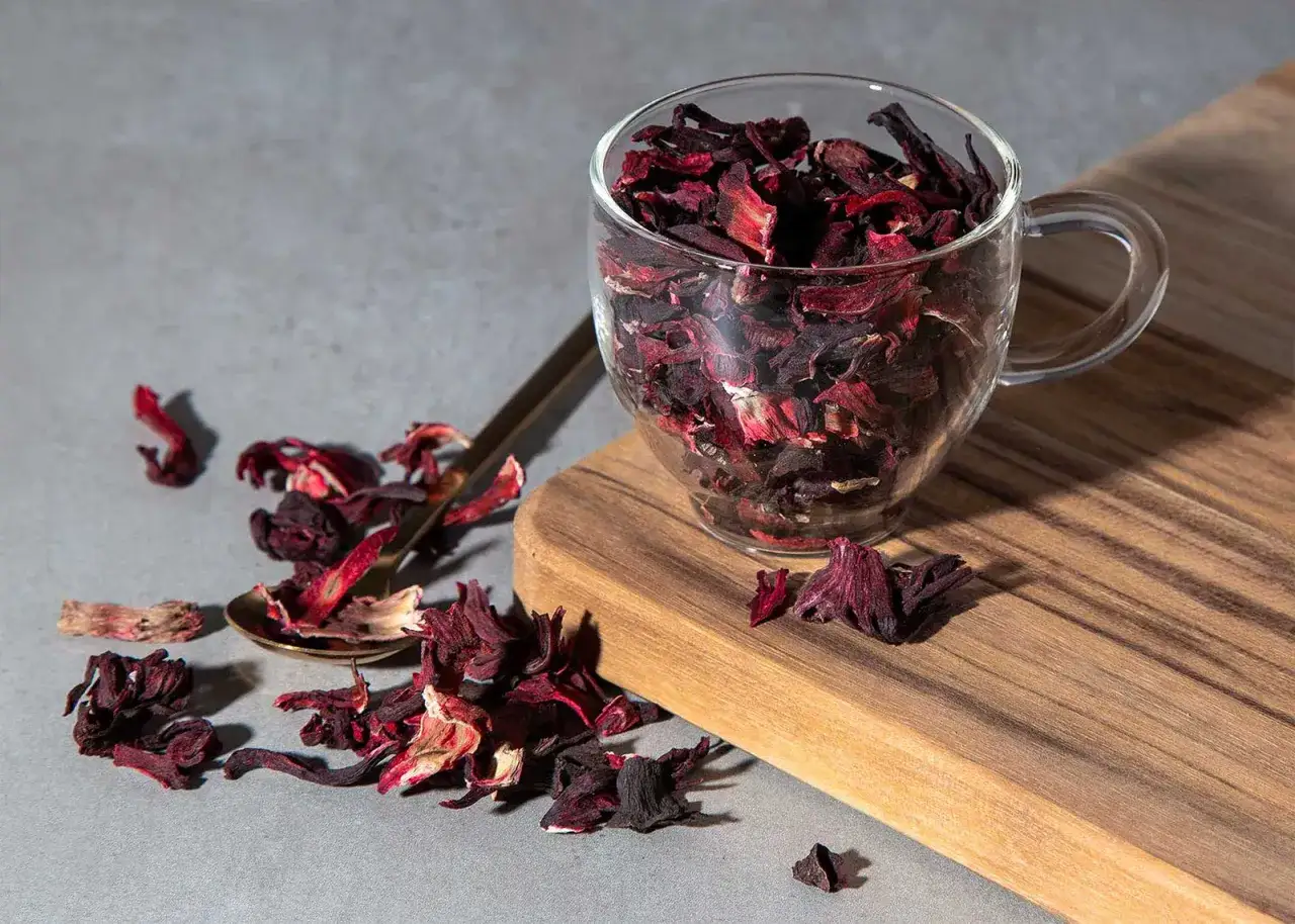 Get ready for the **Cistus Tee Wirkung**! A glass cup overflows with dried hibiscus petals, a golden spoon rests nearby, hinting at the refreshing taste and health benefits.
