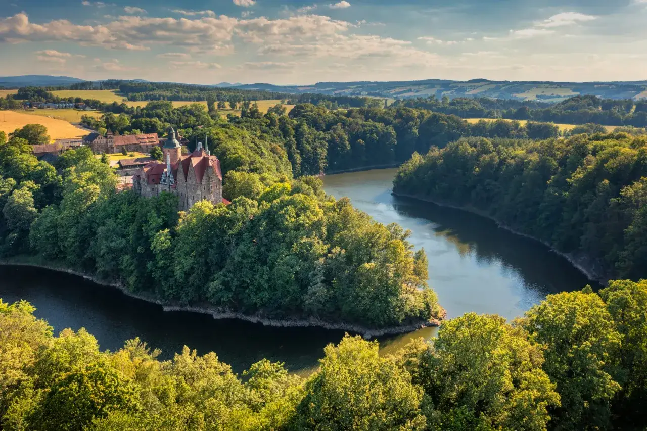 Zamek Czocha, malowniczo położony nad zakolem rzeki, otoczony bujną zielenią.