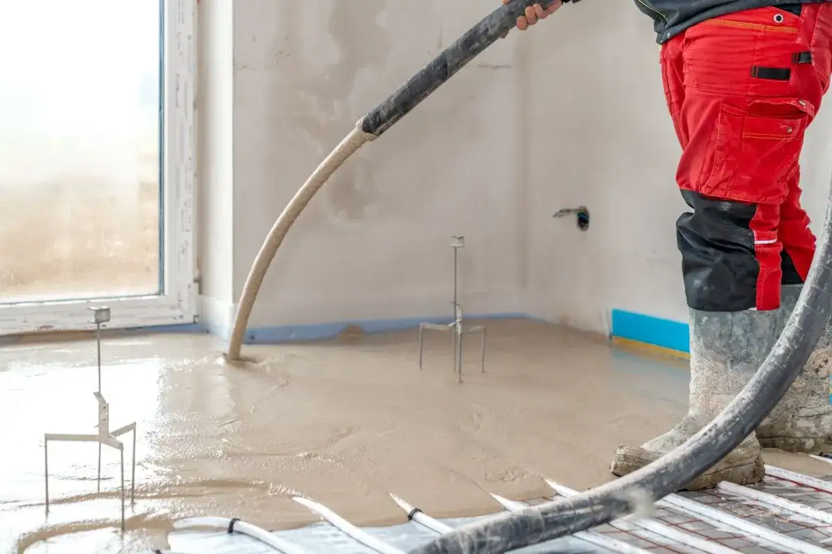 Installazione impianto a pavimento: un operaio versa il massetto. Il costo di un impianto a pavimento &egrave; un investimento per il comfort.