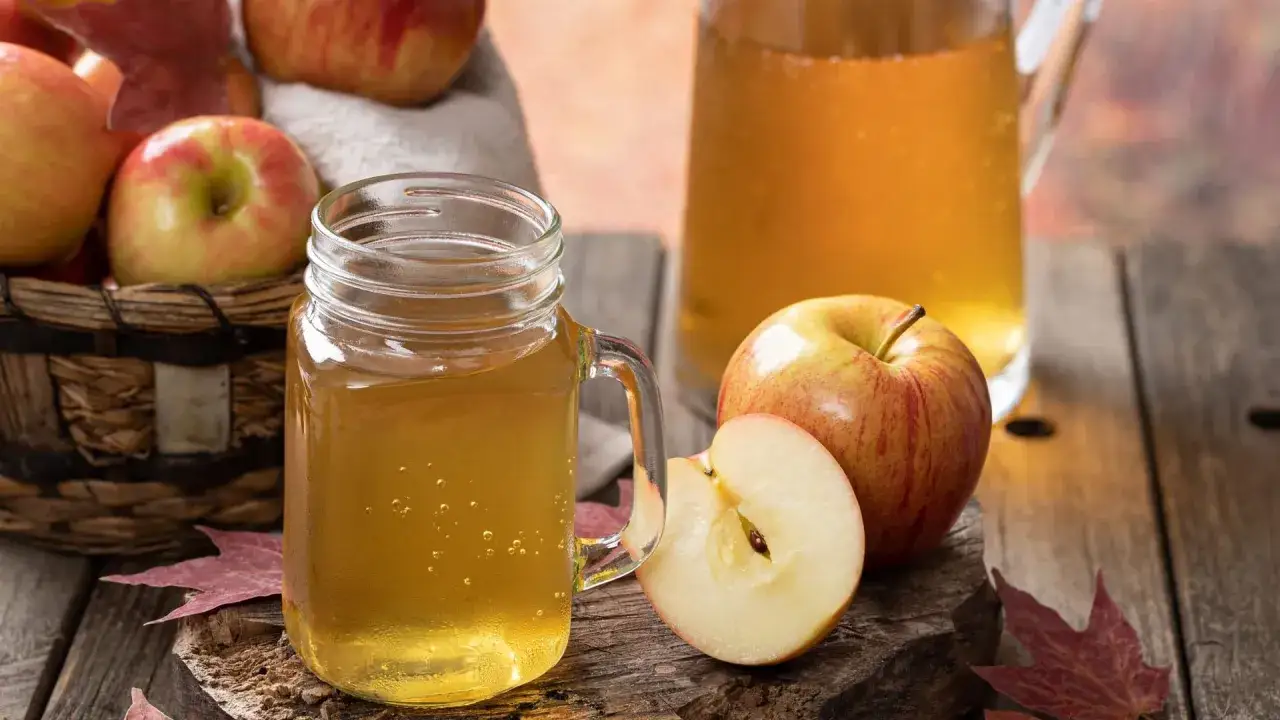 Frischer selbstgemachter Apfelsaft in einem Glas und einer Karaffe, daneben &Auml;pfel und Herbstlaub. Wie lange haltbar ist der Saft?