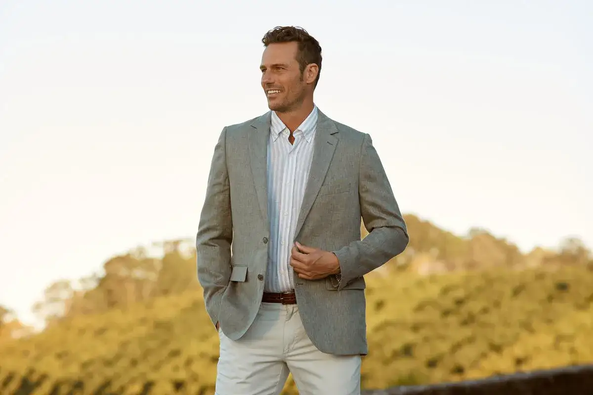 A man in a light grey blazer, striped shirt, and beige pants. This is a great outfit idea for what to wear to an engagement party.