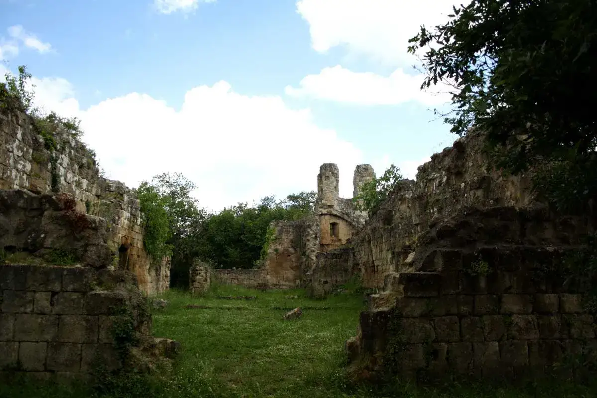 Rovine di Vitozza a Sorano, con mura di pietra antica e vegetazione rigogliosa sotto un cielo azzurro con nuvole bianche.