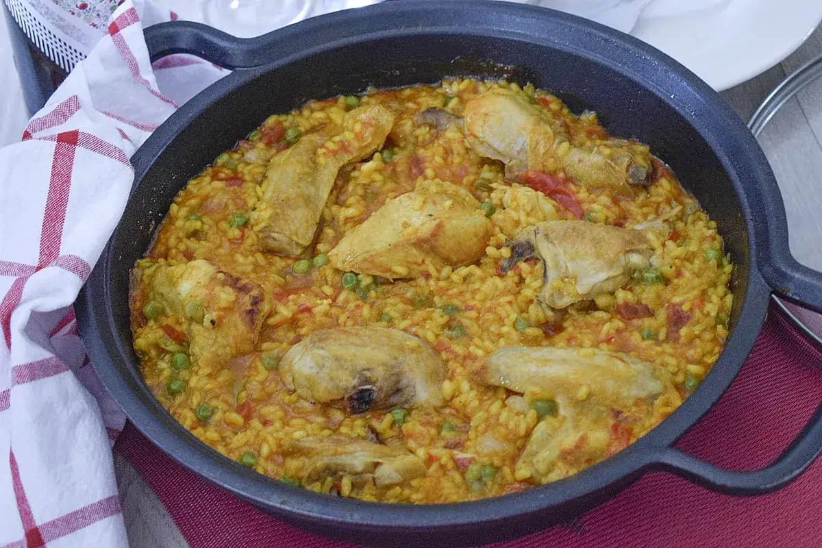 Arroz con pollo de la abuela, un plato casero con trozos de pollo dorado, guisantes y arroz amarillo en una paellera.