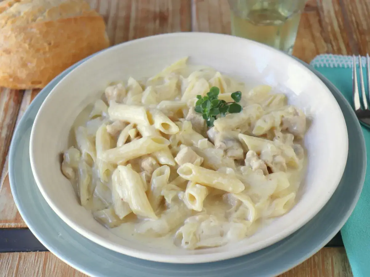 Un plato cremoso de macarrones con nata y trocitos de pollo, decorado con una ramita de tomillo. &iexcl;Un manjar!