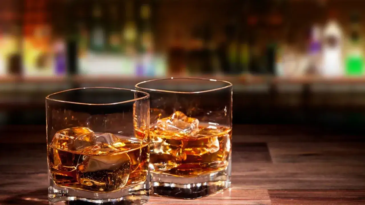 Dwa szklanki z lodem i bursztynowym płynem, idealne na wieczór z whisky z miodem.