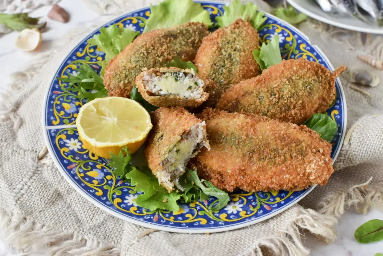 Sarde a beccafico dorate e croccanti, ripiene di un gustoso impasto, servite su un piatto blu decorato con limone e insalata.