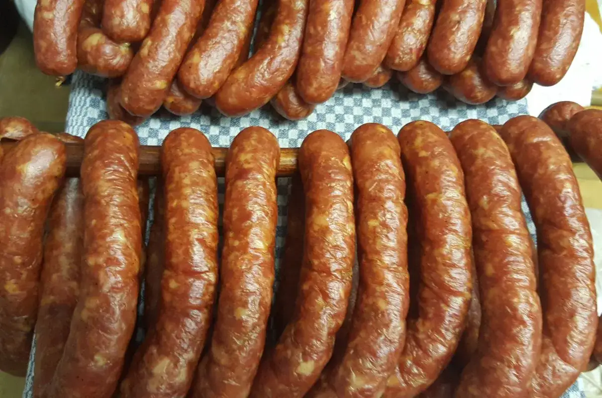 Gotowe do wędzenia, pachnące prawdziwa wiejska kiełbasa przepis. Wędliny wiszą na drewnianych kijach, gotowe do dalszej obróbki.