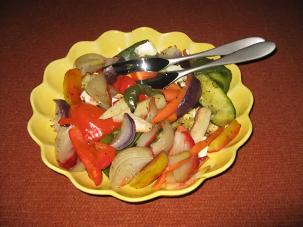 En gul skål med ugnsrostade grönsaker och fetaost. Bland annat paprika, lök, morötter och zucchini.