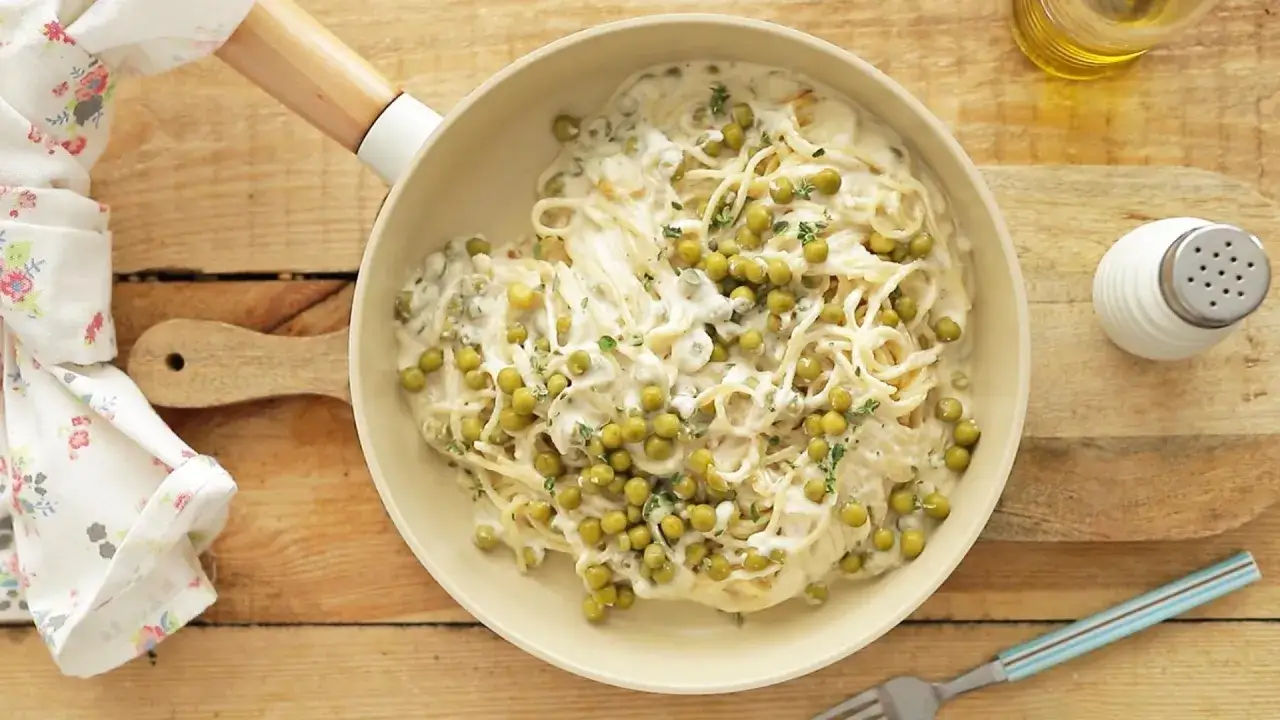 Kremowe spaghetti z groszkiem, pyszna pasta warzywna, podana w kremowym sosie, ozdobiona świeżymi ziołami.