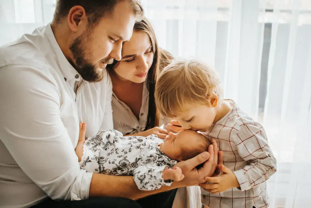 Rodzina w komplecie. Tata trzyma noworodka, mama patrzy z czułością, a starszy brat całuje maluszka. To piękny obrazek z czwartego trymestru życia rodziny.