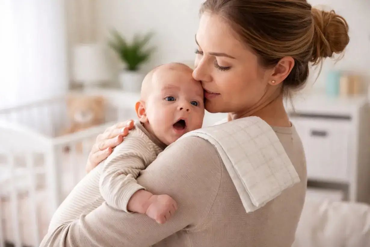 Mamma culla il suo neonato, che ha un piccolo singhiozzo dopo la poppata. La culla e un orsacchiotto sono sullo sfondo.