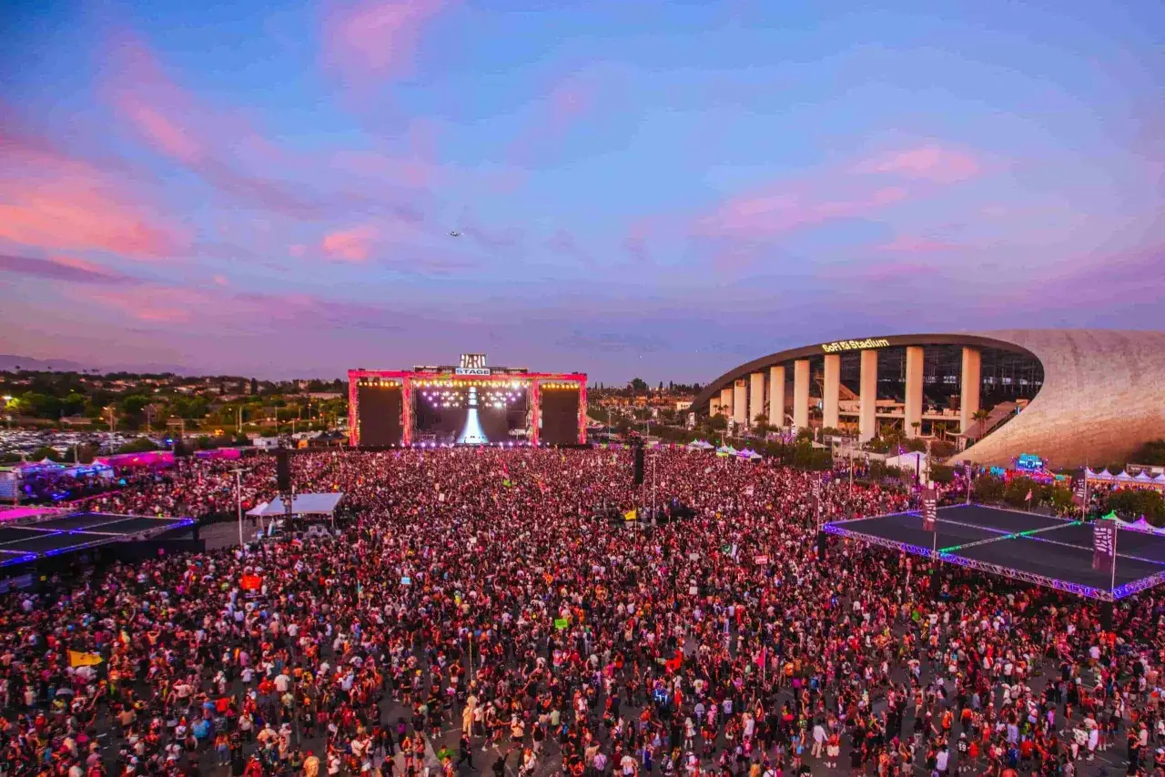 Un'enorme folla partecipa a uno dei tanti festival musicali in Italia, con un palco illuminato e lo stadio SoFi sullo sfondo.