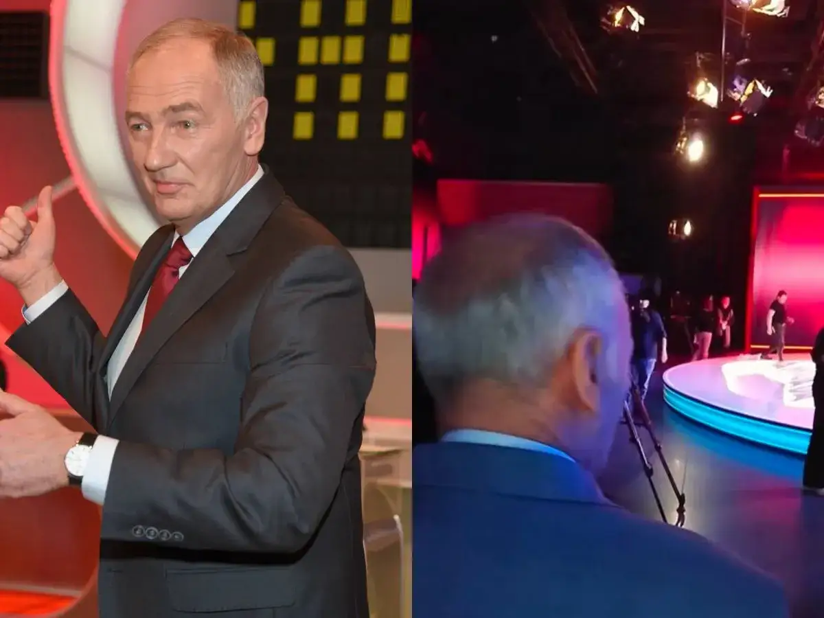 Mężczyzna w garniturze daje kciuk w górę, jakby chciał być zdrowy jak Familiada. W tle widać studio telewizyjne.
