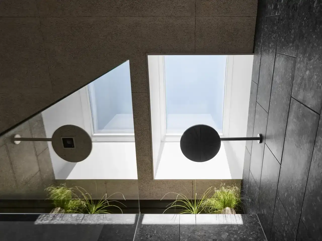 Un bagno cieco illuminato da un lucernario zenitale. Doccia moderna con soffione a pioggia e piante verdi.