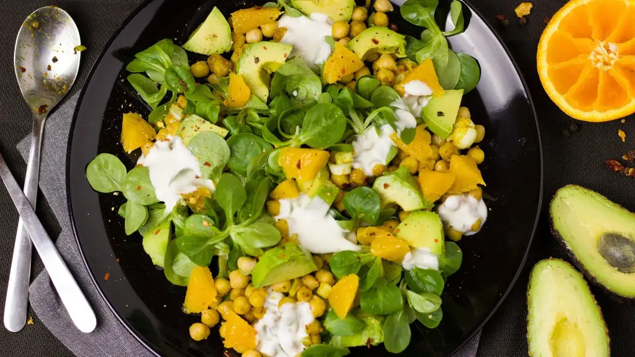 Deliziosa insalata di legumi con ceci, avocado, arancia e un dressing cremoso. Un piatto fresco e nutriente.