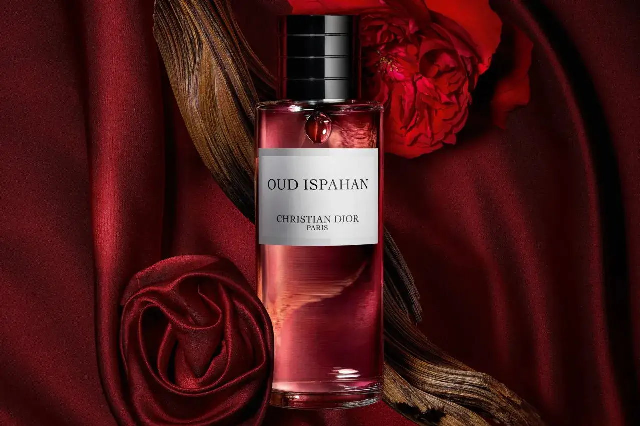 Elegancka butelka Dior Oud Ispahan na tle czerwonego jedwabiu i róży.