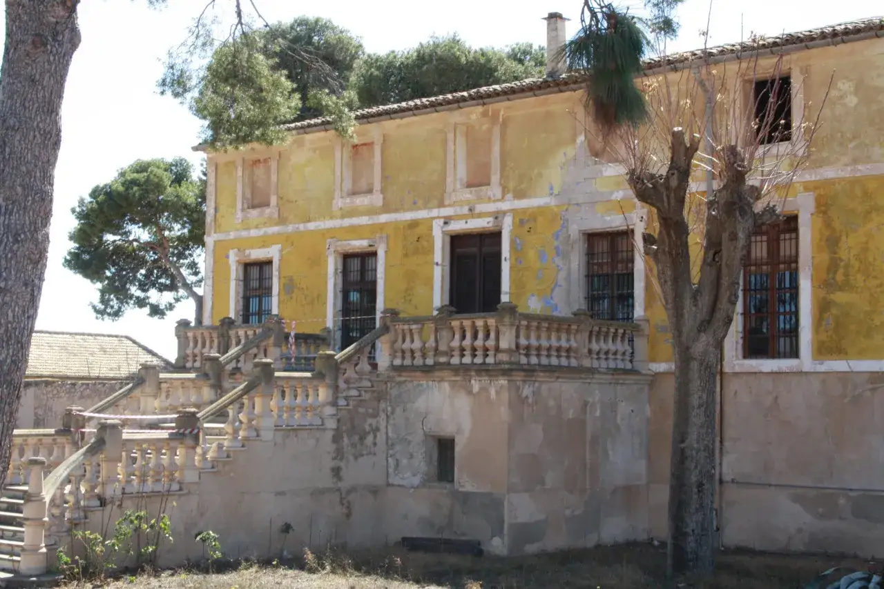 Fachada de la casa Jorge Juan en Novelda, con escalinata de piedra y árboles secos.