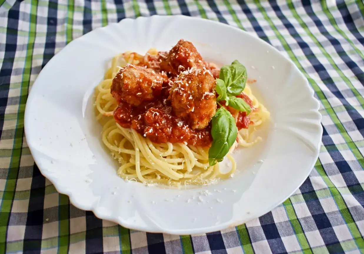 Pyszne spaghetti z klopsikami w sosie pomidorowym, posypane parmezanem i udekorowane listkami bazylii.