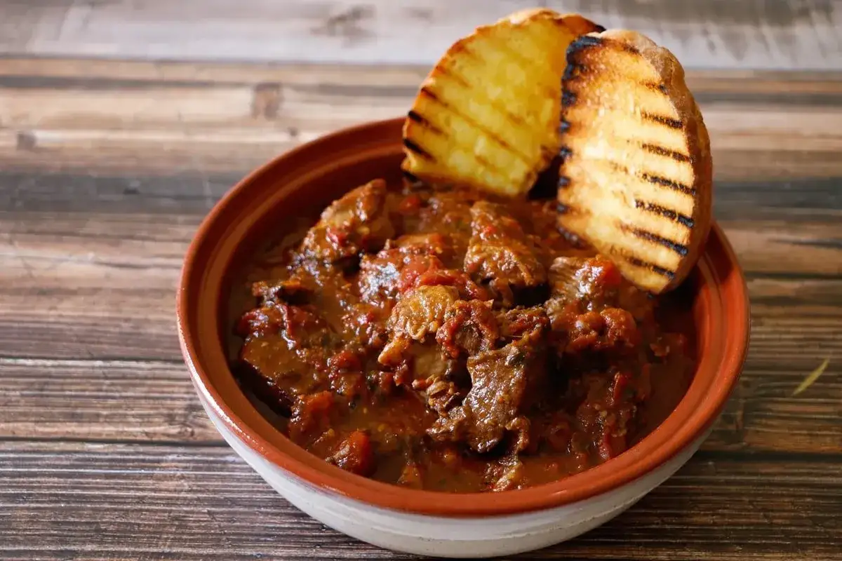 Un saporito spezzatino di cinghiale, uno dei piatti tipici toscani, servito in una ciotola di terracotta con fette di pane abbrustolito.