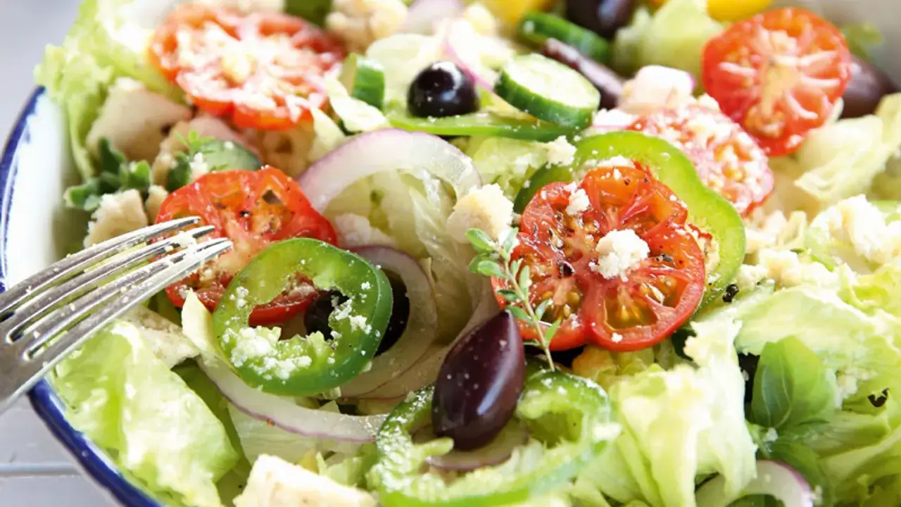 Ensalada griega fresca con lechuga, tomate, pepino, pimiento verde, cebolla morada, aceitunas negras y queso feta desmoronado.