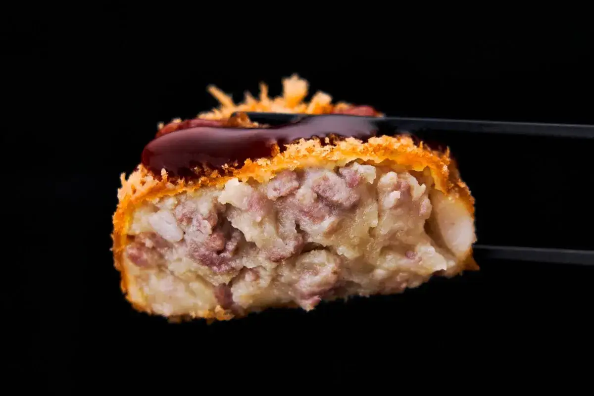 A delicious potato croquette, crispy on the outside and filled with savory ingredients, is drizzled with a rich sauce.