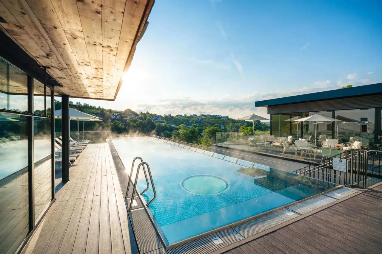 Ein luxuri&ouml;ser Pool mit Dampf und Blick auf eine h&uuml;gelige Landschaft. Perfekt f&uuml;r einen entspannten Urlaub in NRW.