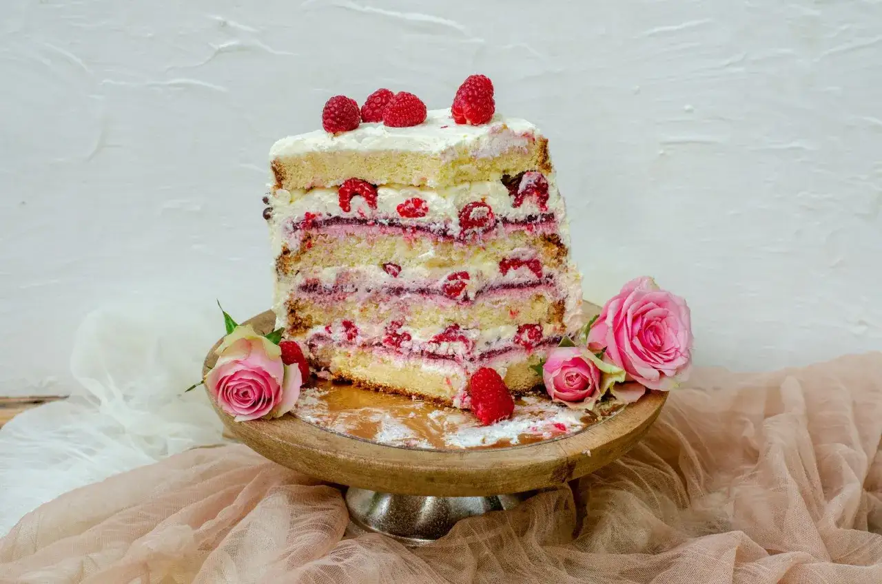 Un gâteau d'anniversaire facile et bluffant, aux multiples couches de génoise, crème et framboises, décoré de roses roses.