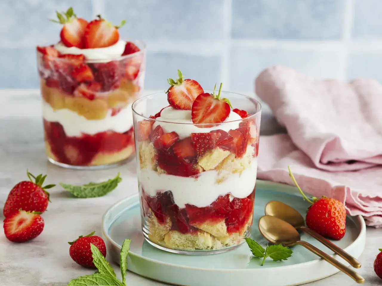 Zwei Gläser mit Erdbeer Tiramisu, geschichtet mit Biskuit, Sahne und frischen Erdbeeren, garniert mit Erdbeeren und Minze.