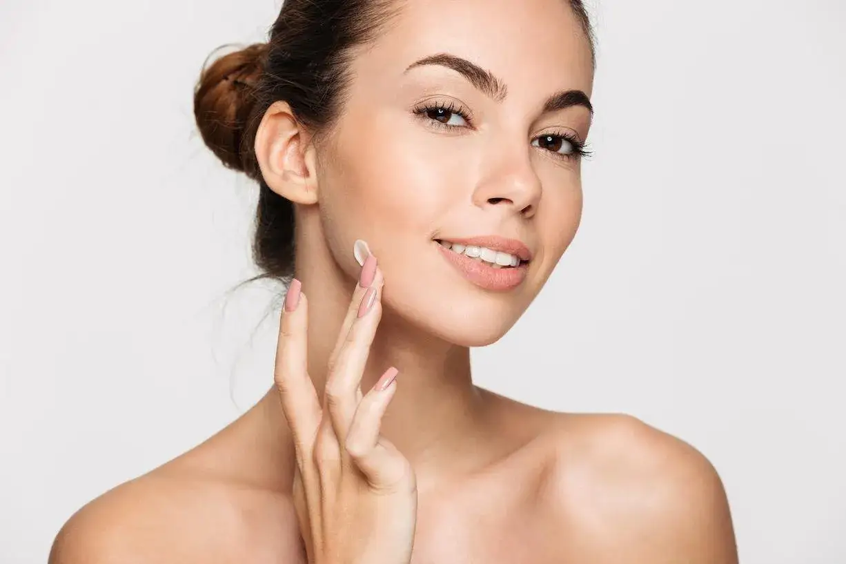 Mujer sonriente aplica crema en su rostro, logrando un look natural sin maquillaje.