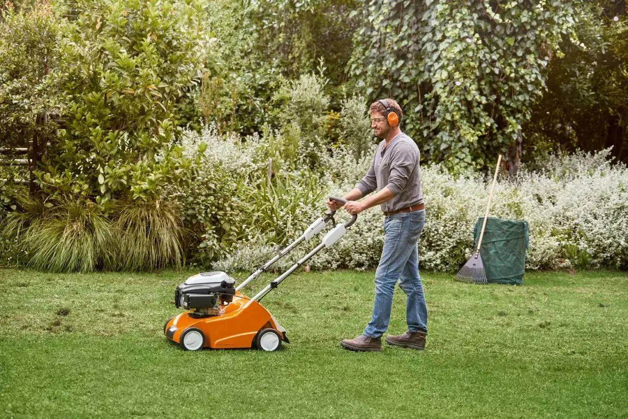 Un homme scarifie sa pelouse avec une machine orange. C'est le bon moment quand scarifier pelouse pour un gazon sain.