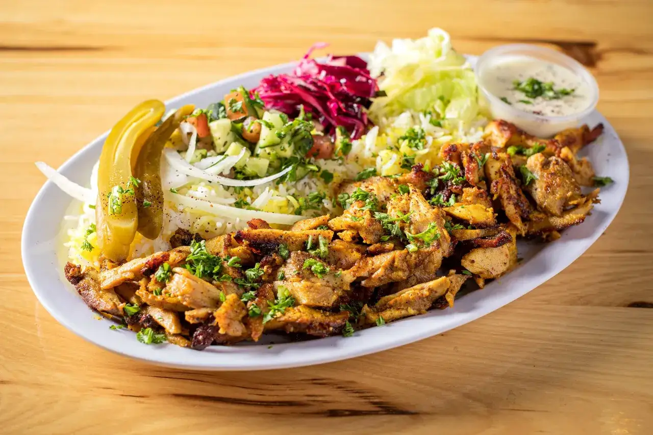 En tallrik med kyckling shawarma, ris, sallad, pickles och en vit sås. En härlig måltid!