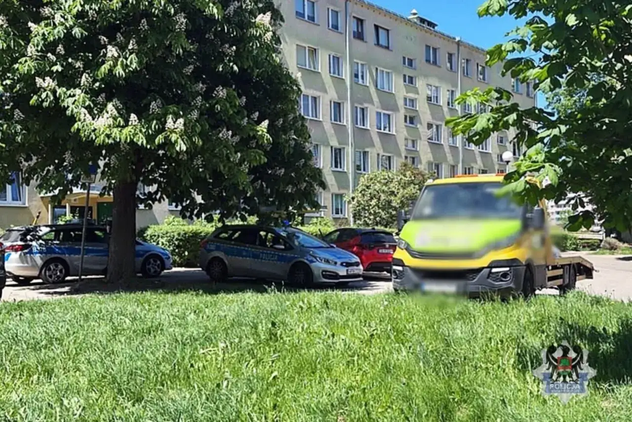 Na osiedlu doszło do kolizji drogowej. Widać radiowozy policyjne, czerwony samochód i żółty pojazd pomocy drogowej.