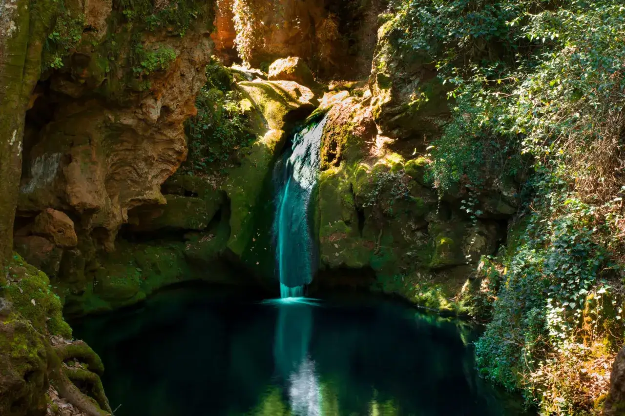Cascada en la ruta de los Baños de Popea, rodeada de rocas cubiertas de musgo y vegetación exuberante.