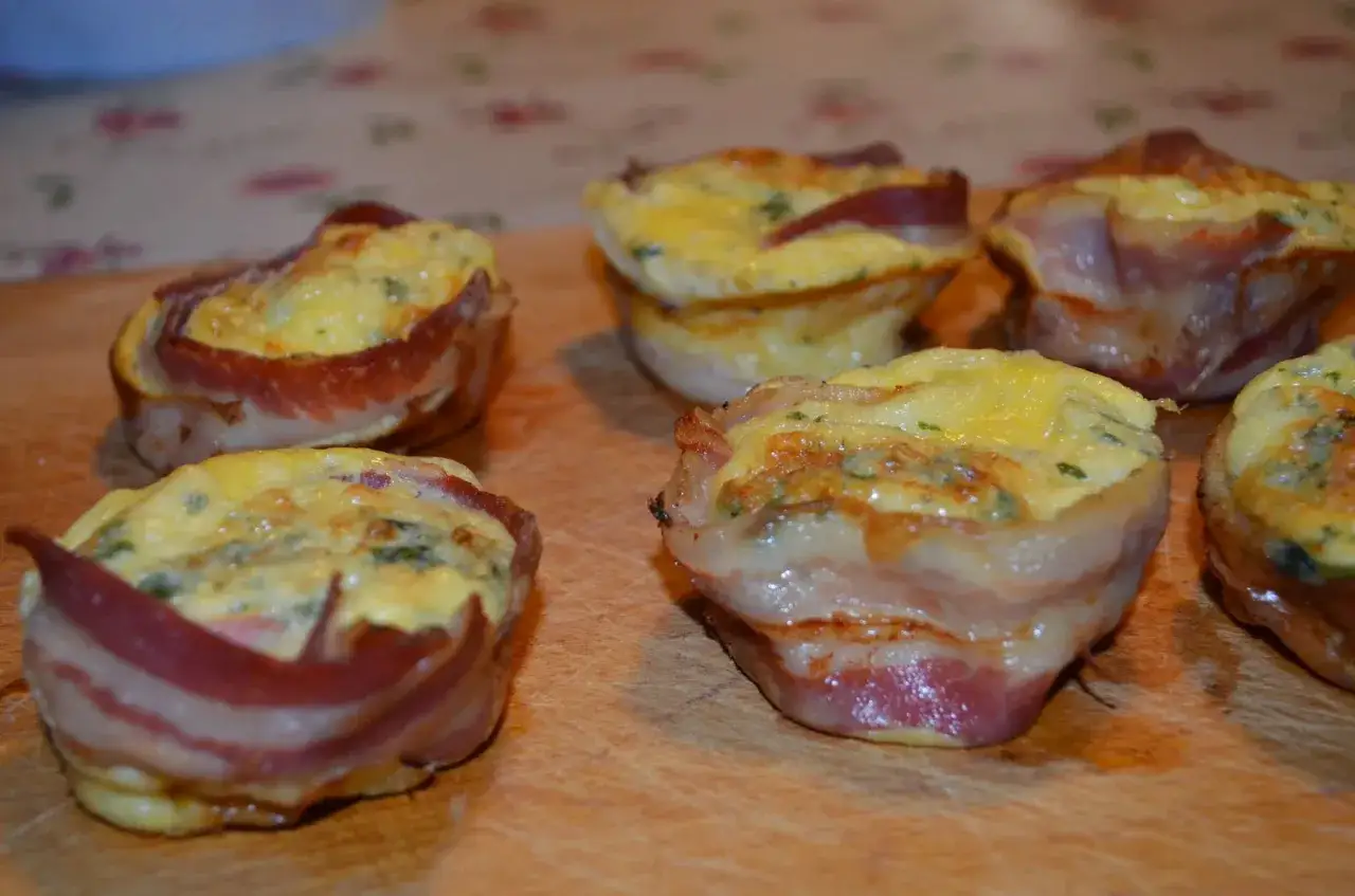 Deliziosi muffin salati con uova e bacon, cotti alla perfezione su un tagliere di legno.
