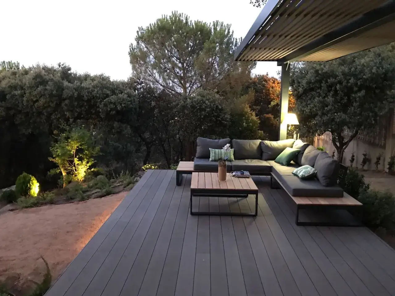 Terraza moderna con sof&aacute; modular y mesa de centro sobre el mejor suelo para exterior. Iluminaci&oacute;n ambiental y vegetaci&oacute;n exuberante.