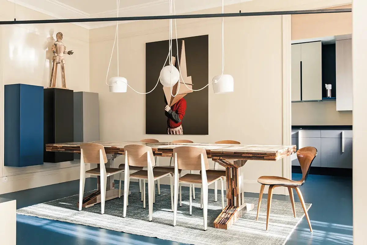 Ingresso su sala da pranzo con tavolo in legno grezzo, sedie moderne e un quadro surreale.