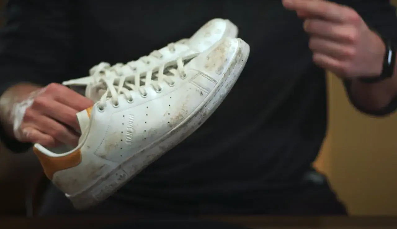 Mani sporche di sapone che puliscono scarpe Stan Smith bianche e sporche. Scopri come lavare le Stan Smith per farle tornare come nuove.